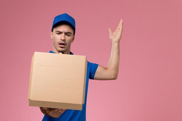 male courier in blue uniform holding delivery box of food on pink, uniform service delivery