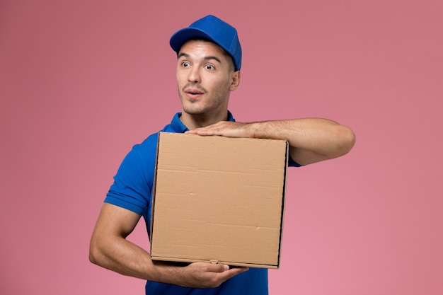 Corriere maschio in uniforme blu che tiene la scatola di consegna di cibo in posa su rosa, consegna del servizio uniforme lavoratore di lavoro