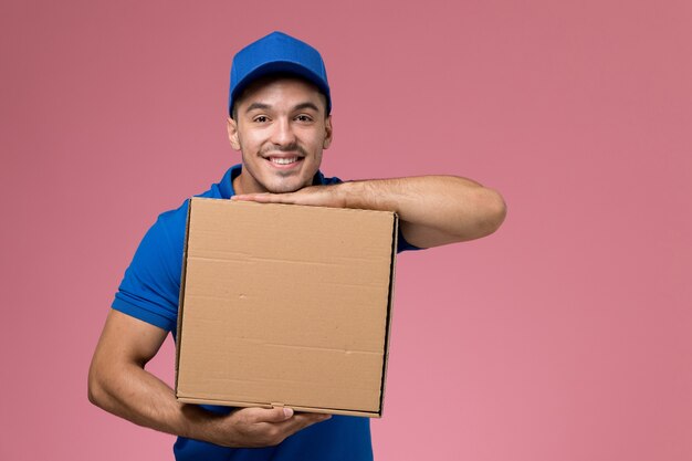 ピンクに微笑んでいる食品の配達ボックスを保持している青い制服を着た男性の宅配便、労働者の制服サービスの配達