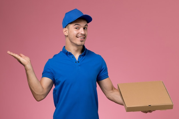 курьер-мужчина в синей форме держит коробку с едой с улыбкой на розовом, служба доставки униформы