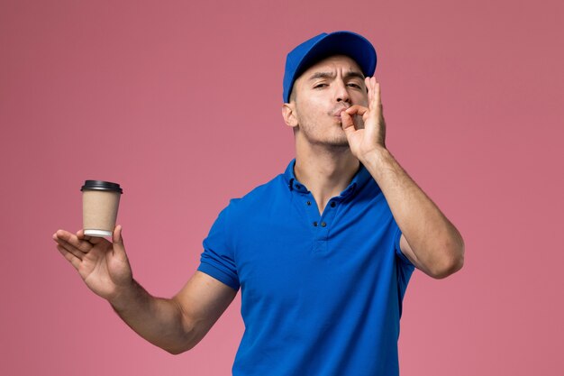 male courier in blue uniform holding delivery coffee cup on pink, uniform job worker service delivery