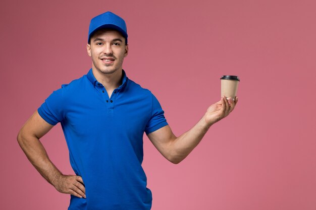 male courier in blue uniform holding delivery coffee cup on pink, uniform service delivery