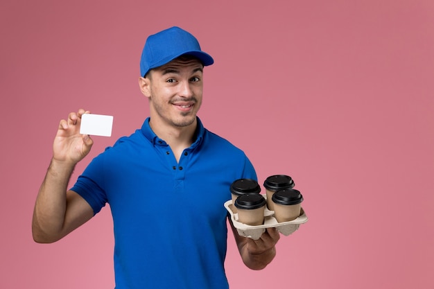 Corriere maschio in uniforme blu che tiene le tazze di caffè di consegna e carta sulla consegna rosa, uniforme del servizio del lavoratore di lavoro