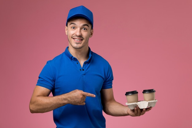 male courier in blue uniform holding delivery coffee cups on pink, uniform service job delivery
