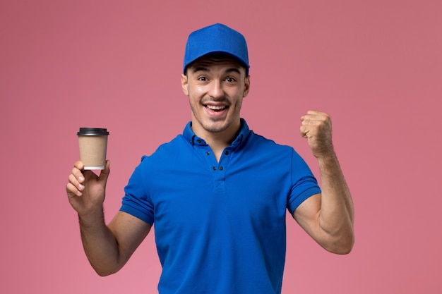 male courier in blue uniform holding delivery coffee smiling on pink, uniform service job delivery