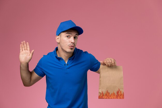male courier in blue uniform holding delivery food package on pink, job worker uniform service delivery