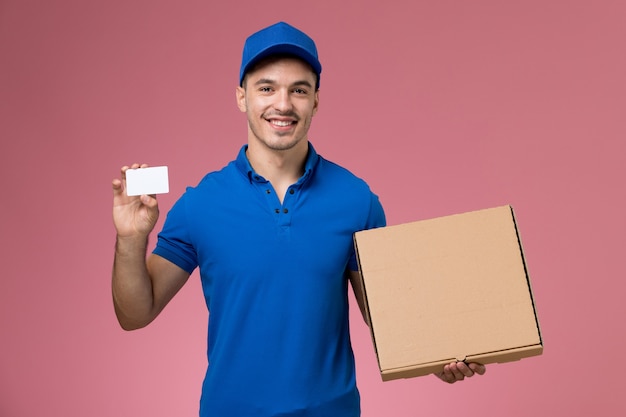 male courier in blue uniform holding food box and card on pink, job uniform service delivery worker