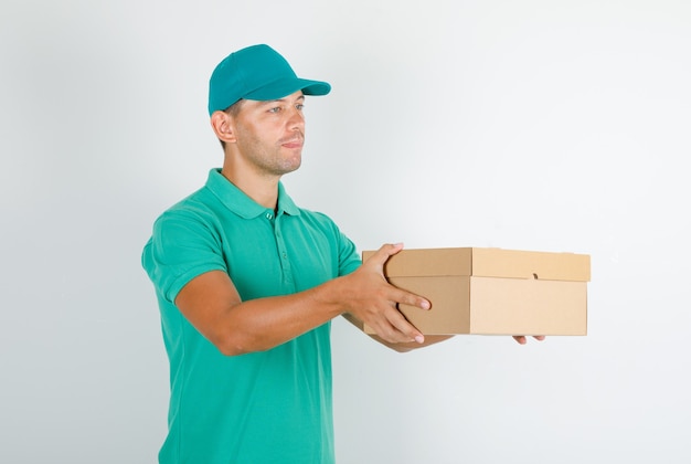 Курьер-мужчина в зеленой футболке с кепкой, доставляющей картонную коробку