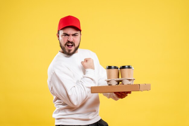 male courier holding delivery food box and coffee on yellow