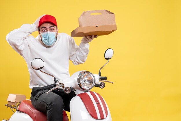 male courier in mask on bike holding food box on yellow