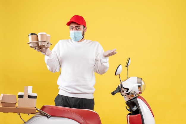 Male courier in mask holding coffee on the yellow