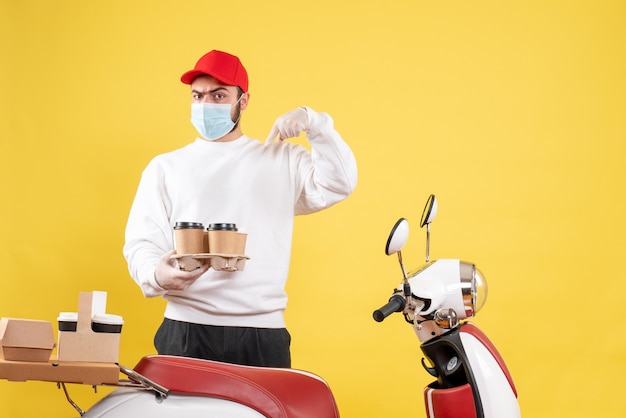 male courier in mask holding coffee on yellow