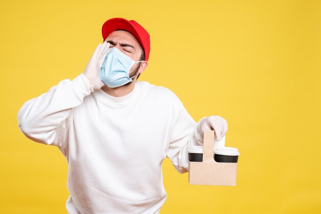 male courier in mask holding delivery coffee calling someone on yellow