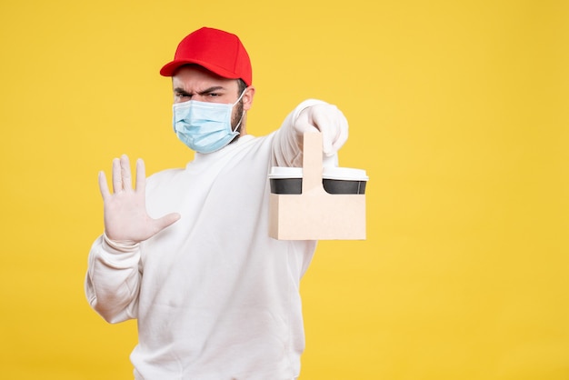 male courier in mask holding delivery coffee on yellow