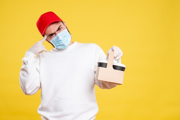 male courier in mask holding delivery coffee on yellow