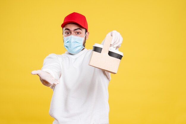 male courier in mask holding delivery coffee on yellow