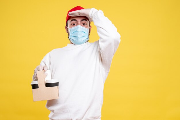 male courier in mask holding delivery coffee on yellow