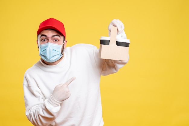 male courier in mask holding delivery coffee on yellow