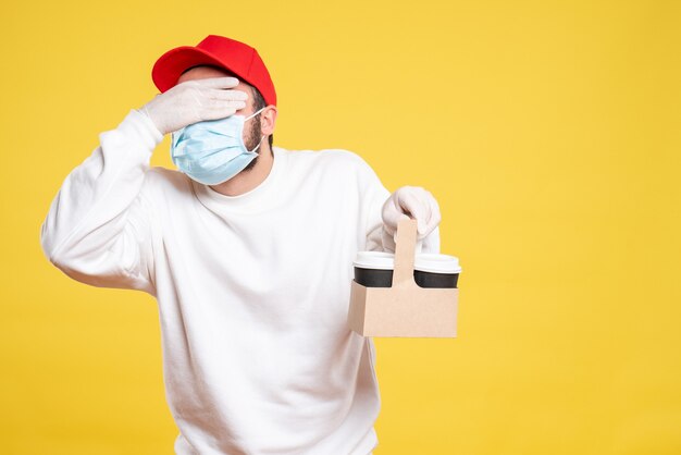 male courier in mask holding delivery coffee on yellow