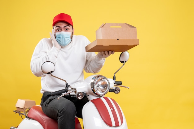 Male courier in mask holding food box on yellow