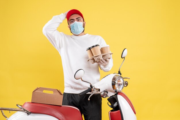 male courier in sterile mask holding delivery coffee on yellow