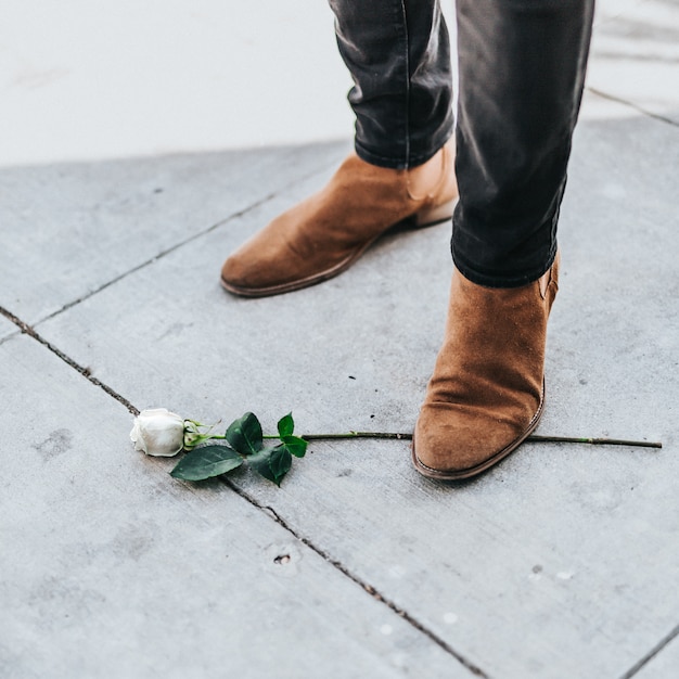 Foto gratuita maschio in stivali da cowboy in piedi su un unico ramo di rosa bianca