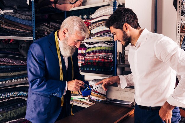 Male customer selecting thread spool with male fashion designer in his shop