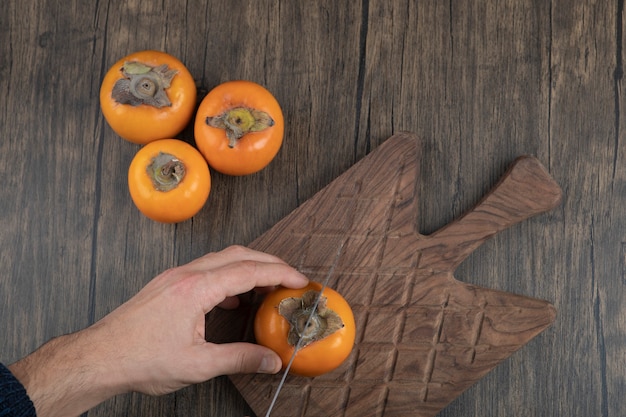 Free photo male cuts persimmon fruit into two pieces on wooden surface