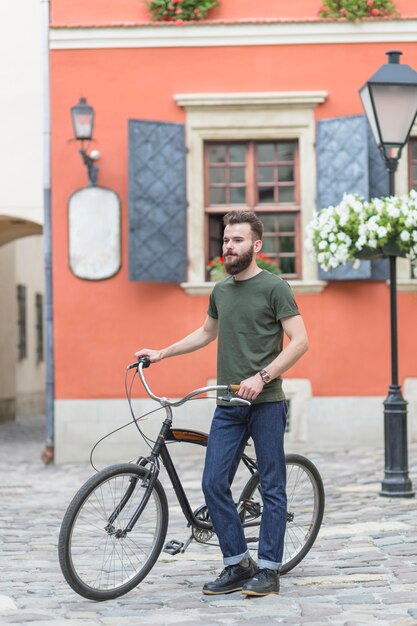 Male cyclist standing with his bicycle in front of building