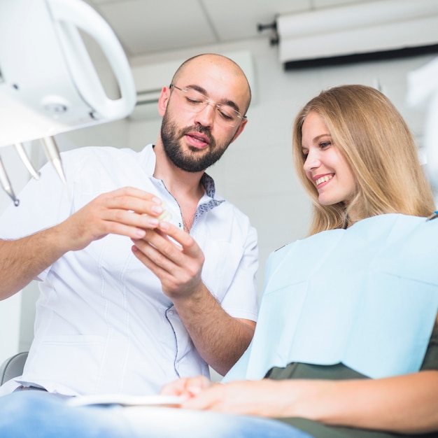 Male dentist showing dental jaw to happy female patient