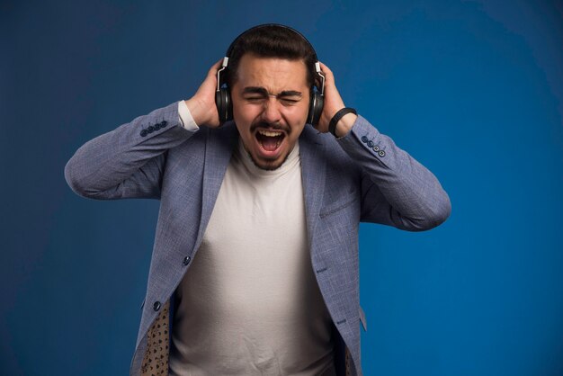 Male dj in grey suit wearing headphones with high volume and screaming. 