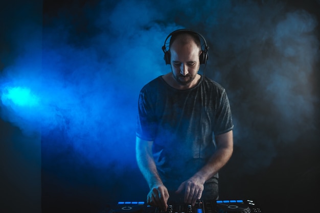 Male DJ working under the blue lights and smoke in a studio against a dark