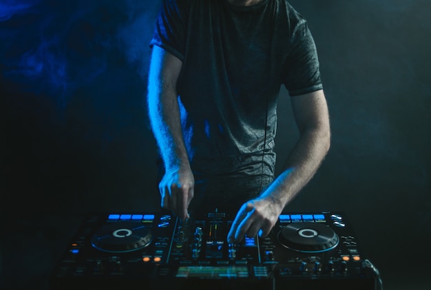 Male DJ working under the lights and smoke against a dark