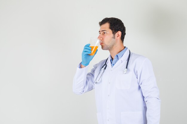 Мужчина-врач пьет фруктовый сок в белом халате, перчатки