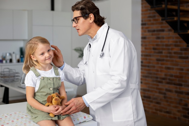 Male doctor examining little girl holding teddy bear toy