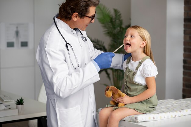 Male doctor examining little girl holding teddy bear toy