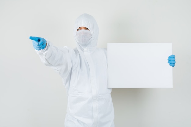 Male doctor holding blank canvas, pointing away in protective suit