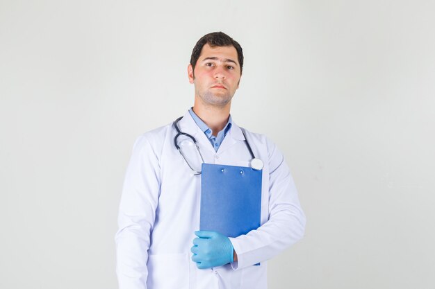 Male doctor holding clipboard in white coat, gloves and looking serious. front view.