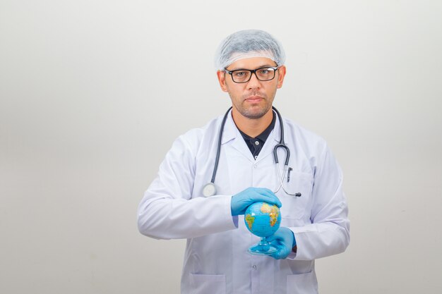 Male doctor holding earth globe in his hands in white coat and hat and looking positive