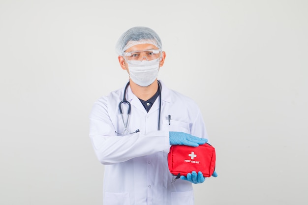 Male doctor holding first aid kit in protective clothes and looking careful