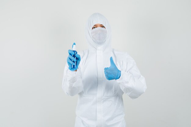 Male doctor holding hand sanitizer, showing thumb up in protective suit