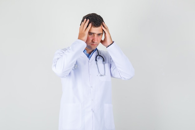 Male doctor holding head with hands in white coat and looking upset