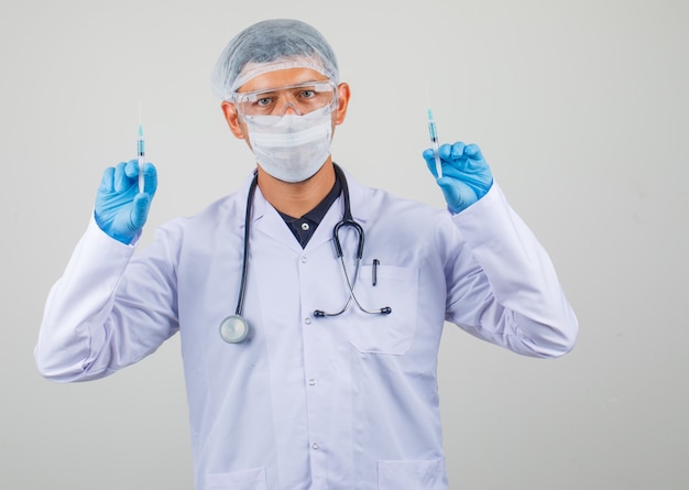 Male doctor holding medical two syringes up in protective clothes