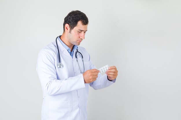 Мужчина-врач держит пачку таблеток в белом халате и выглядит серьезно