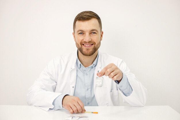 白い背景で隔離のCovid19に対するワクチンを保持している男性医師