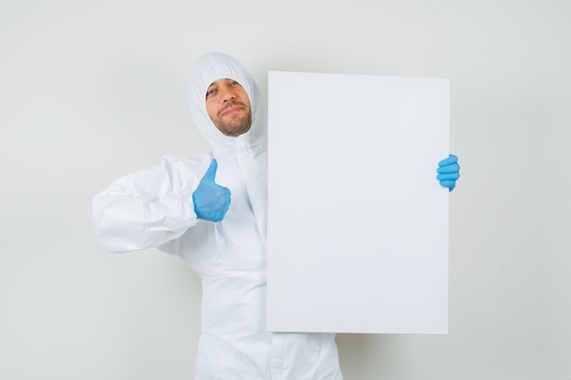 Male doctor holding white board with thumb up in protective suit