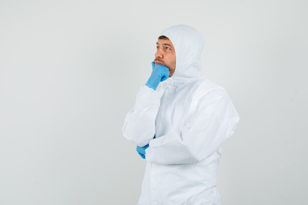 Male doctor looking up with hand on chin in protective suit