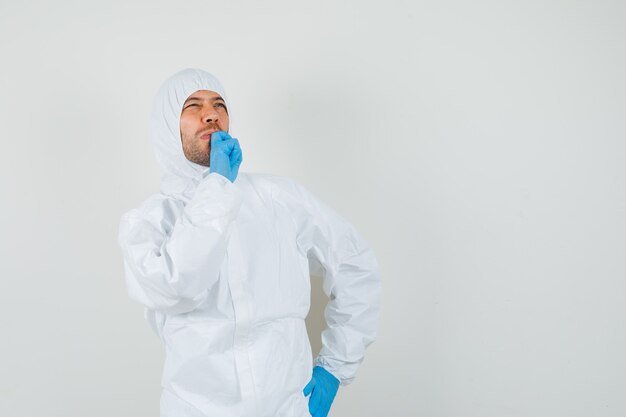 Male doctor looking up with hand on chin in protective suit