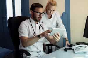 Free photo male doctor and nurse cooperating while examining electronic medical records of a patient in doctor's office