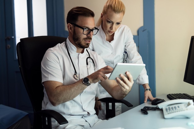 Male doctor and nurse cooperating while examining electronic medical records of a patient in doctor's office